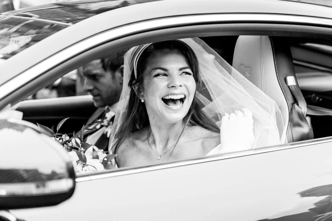 Bride-in-veil-laughs-out-of-the-car-window-on-her-wedding-day