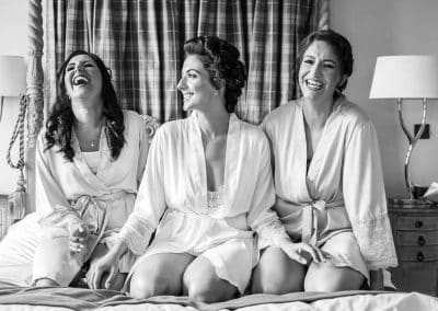 A bride and her bridesmaids sit in matching robes on her bed at Froyle Park Country Park.