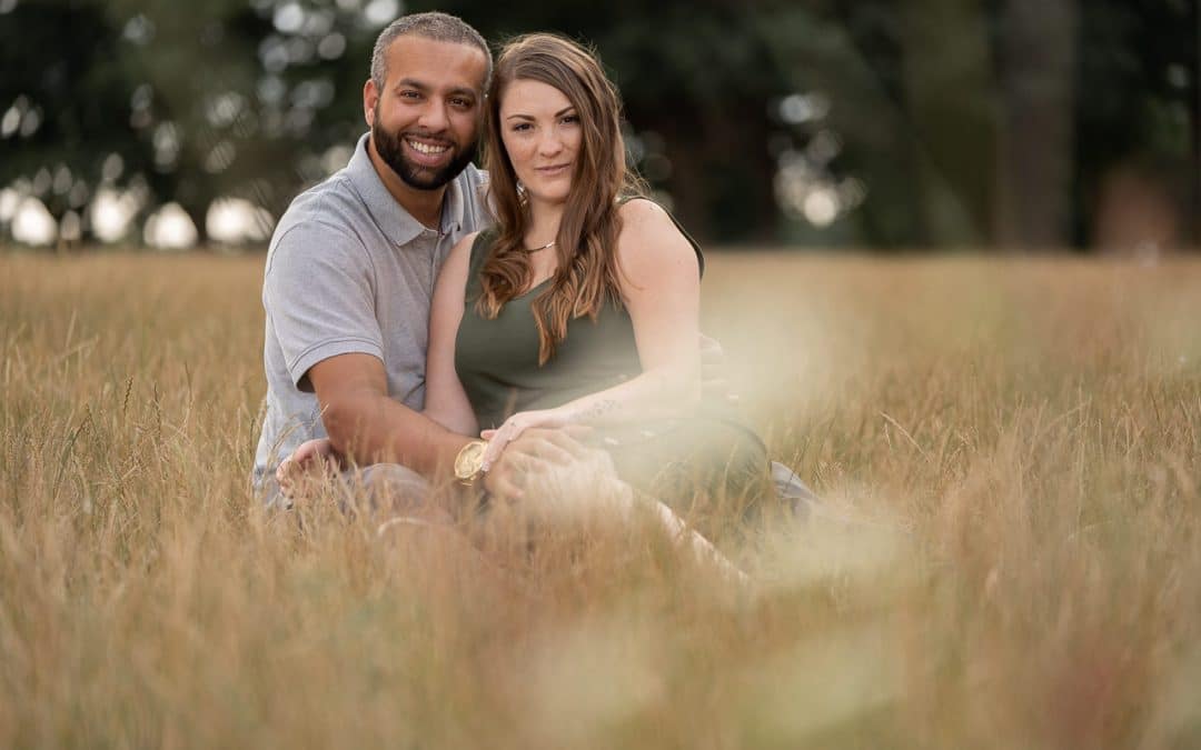 engaged-couple-sitting-in-dry-long-grass-in-a-field-at-the-grove-hertfordshire