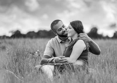 engaged-couple-sitting-in long-grass-black-and-white-photo-at-the-grove-hotel-hertfordshire